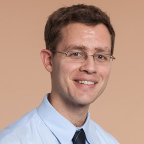 Jim Patterson in a button-up and tie in front of a background. 