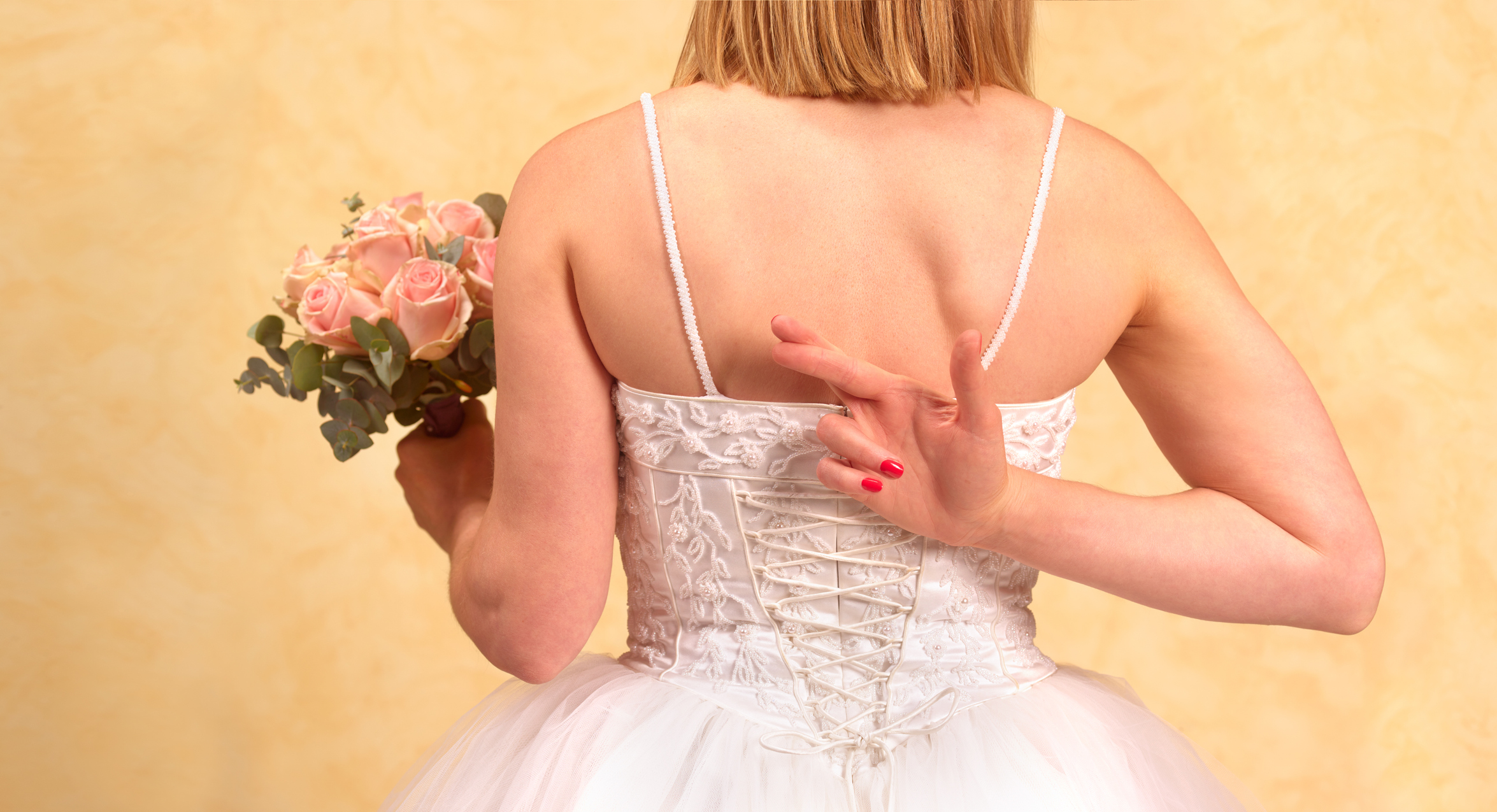 A bride crosses her fingers behind her back holding a bouquet. 
